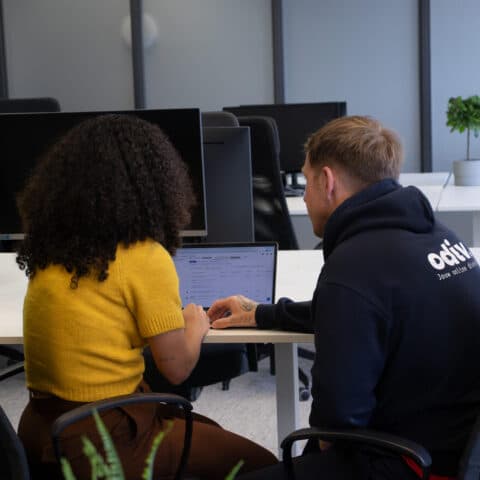 Een vrouw en een man die met hun rug naar de camera zitten en naar een computer kijken