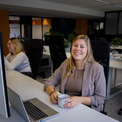 Witte vrouw met kop koffie lachend achter laptop
